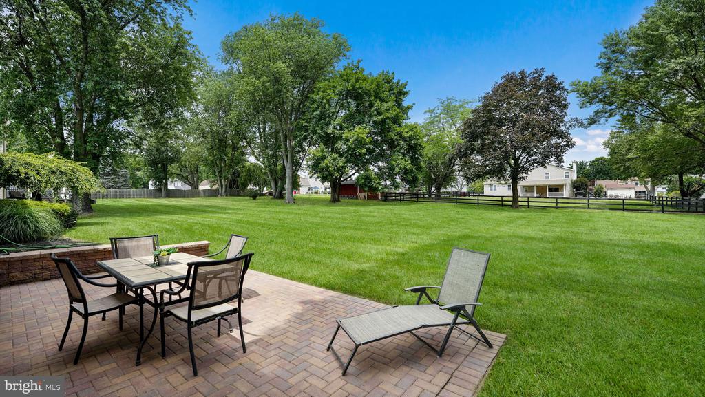 Brick patio with outdoor dining set and chaise lounge overlooking a broad lawn and mature trees.