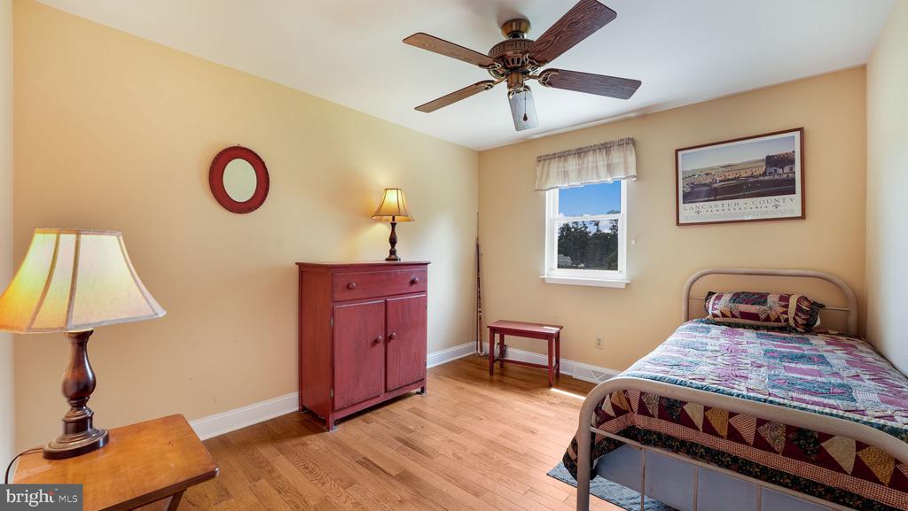 Bedroom with a colorful quilt, red wooden cabinet, hardwood floors, and ceiling fan.