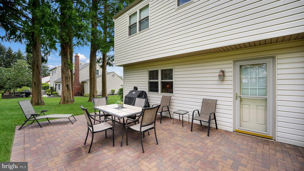 Brick-paver patio with outdoor dining furniture, a grill, and mature trees.