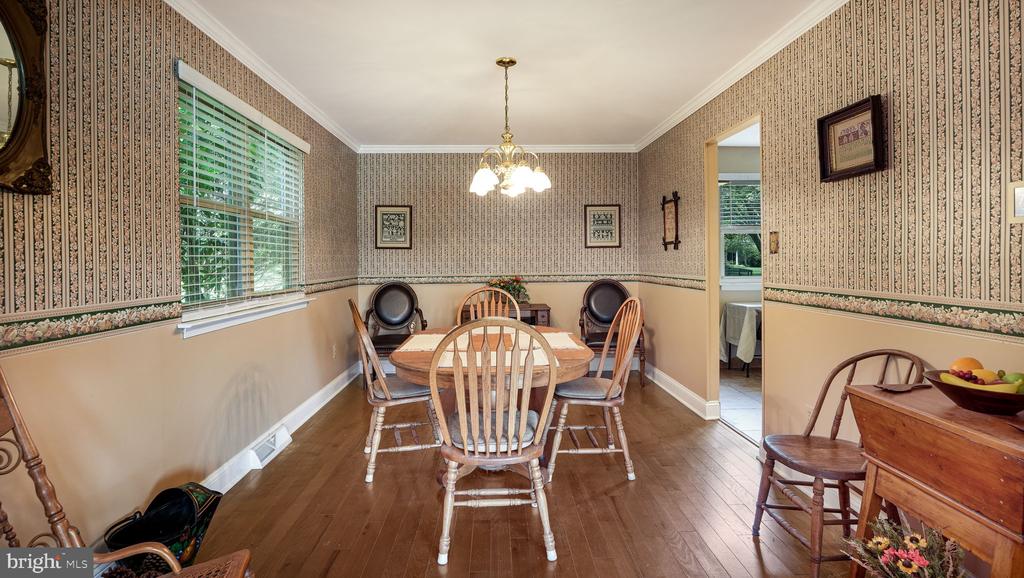 Dining room with a wooden table, spindle-back chairs, patterned wallpaper, and hardwood floors.