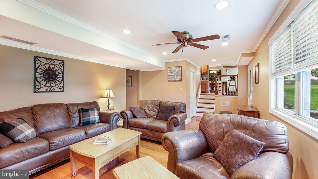 Living room with brown leather sofas, hardwood floors, a ceiling fan, and wide windows.