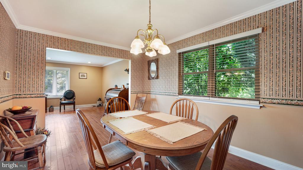 Dining room with a round wooden table, patterned wallpaper, brass chandelier, and large window.