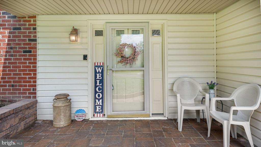 Covered front porch with a wreath on the door, welcome sign, and two white chairs.
