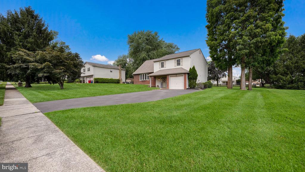 Two-story home with an attached garage, broad lawn, driveway, and mature trees.