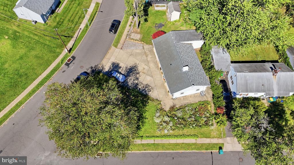 Aerial view of a house, driveway, lawn, and tree-lined street.