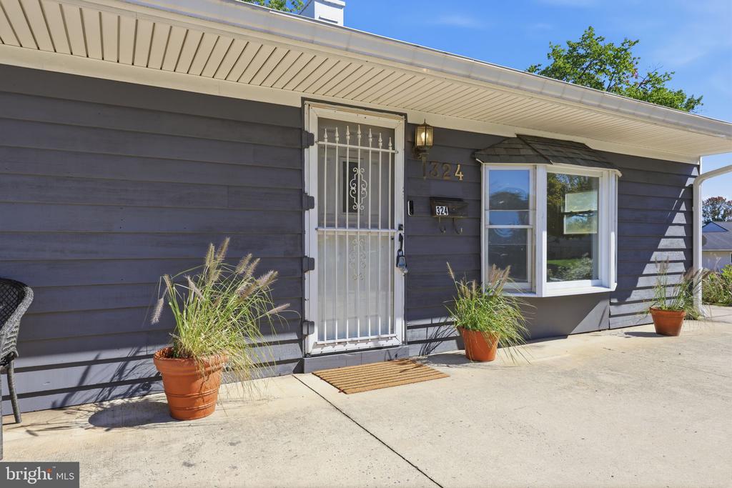 Single-story home entrance with gray siding, white security door, address 324, and potted grasses.