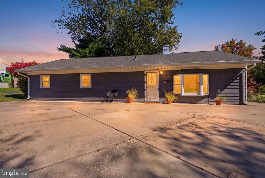 Single-story dark-sided ranch with a broad concrete driveway and warmly lit windows at dusk.