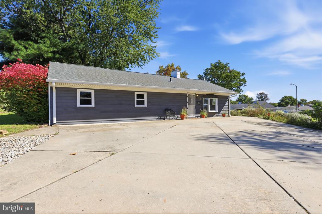 Single-story gray home beside a broad concrete driveway, framed by mature trees and flowering shrubs.