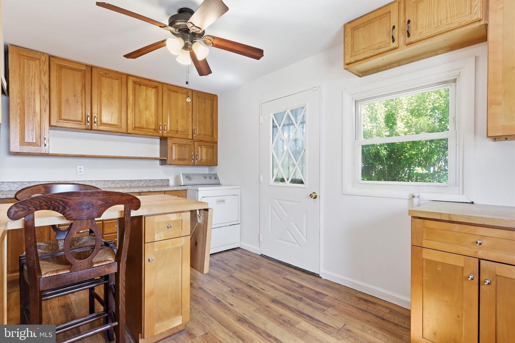 Kitchen with honey-colored wood cabinets, a small table, and a white back door.