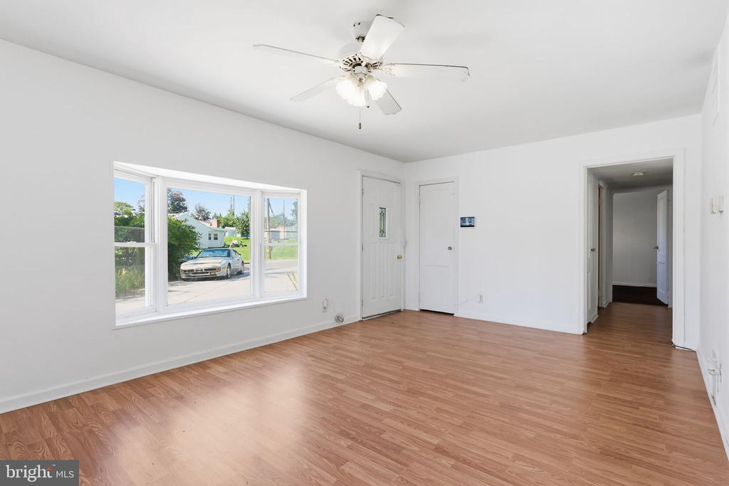 Empty room with light wood-look flooring, a ceiling fan, and a wide street-facing window.