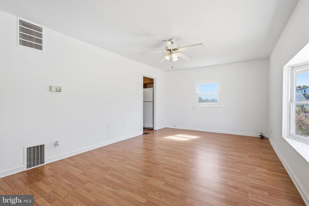 Vacant living room with light wood flooring, a ceiling fan, and large windows.