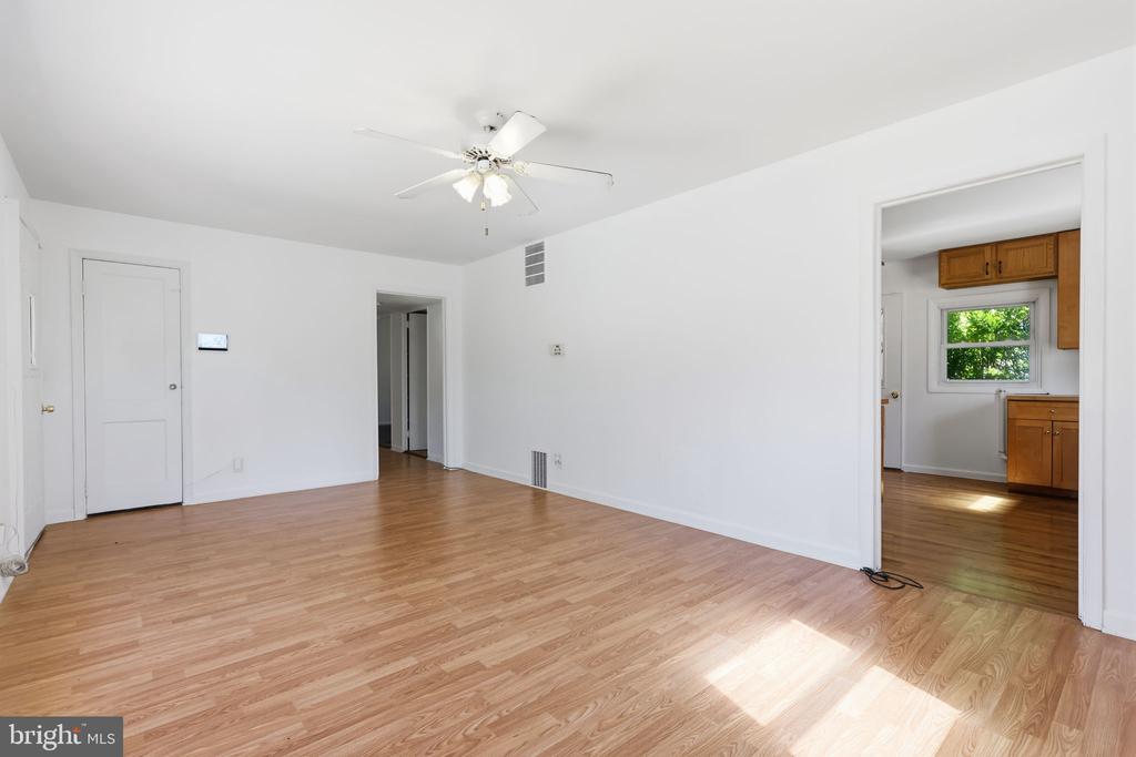 Vacant room with light wood floors, ceiling fan, and doorway to a kitchen.