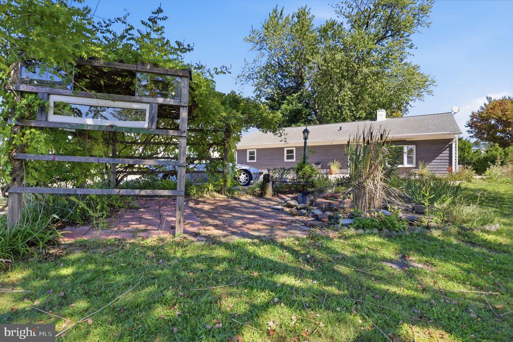 Single-story gray home behind a brick patio and garden with mature trees.
