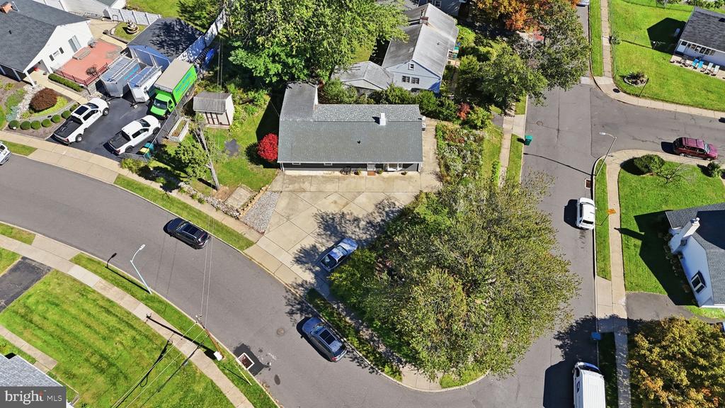 Aerial view of a single-story house with a driveway, yard, and mature trees.
