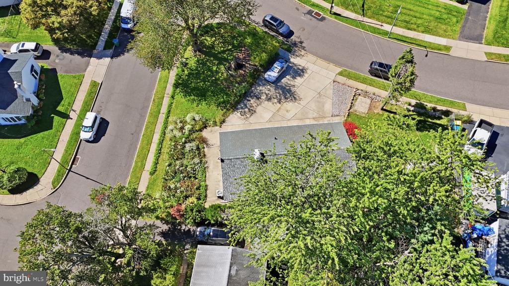 Aerial view of a tree-covered home on a corner lot beside a paved driveway.