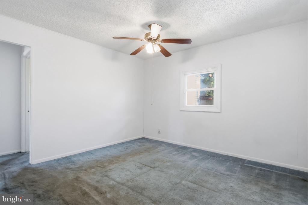 Vacant bedroom with gray carpet, a ceiling fan, and a small window.