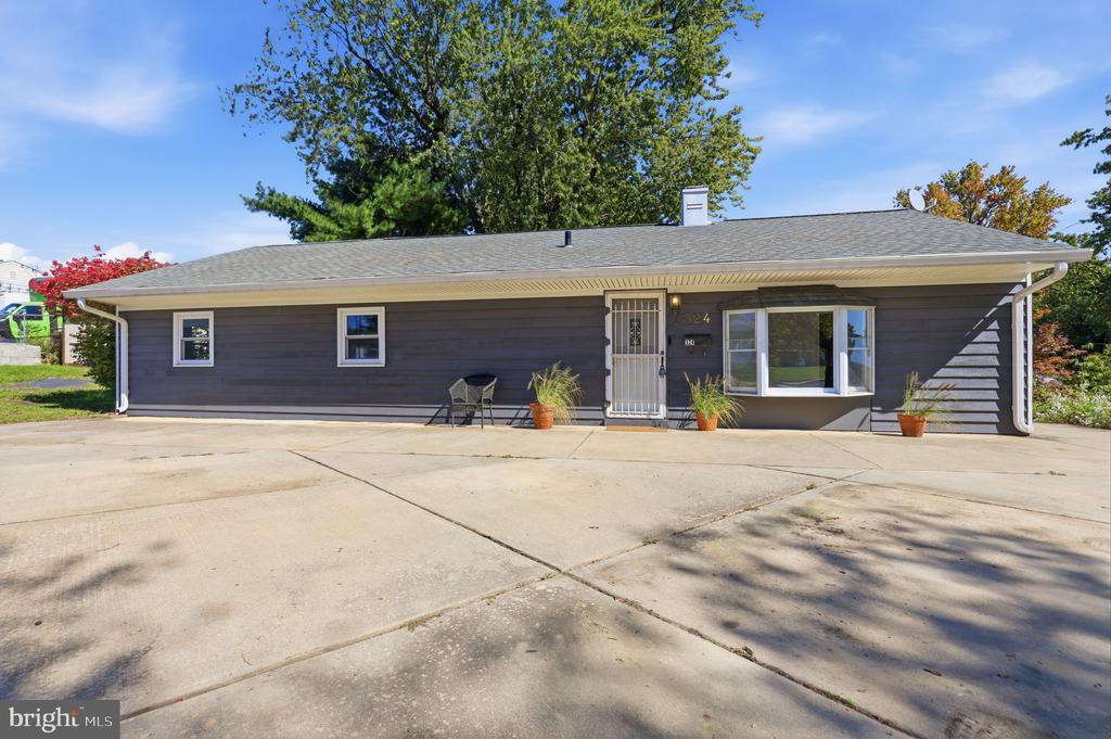Single-story gray home with white-trimmed windows, potted plants, and a wide concrete driveway.