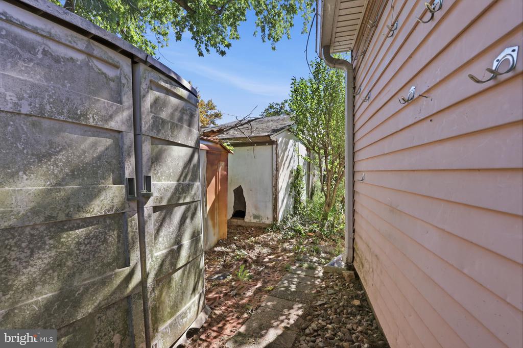 Narrow side yard with a stone path between the house and a weathered privacy fence.