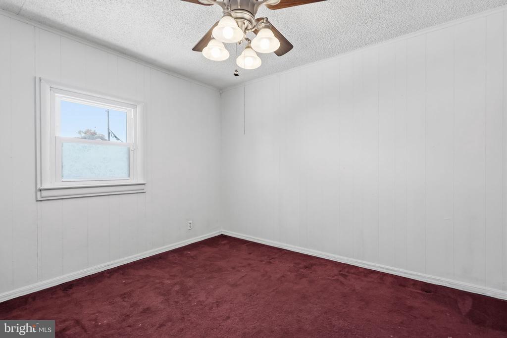 Empty room with burgundy carpet, white paneled walls, and a ceiling fan with lights.