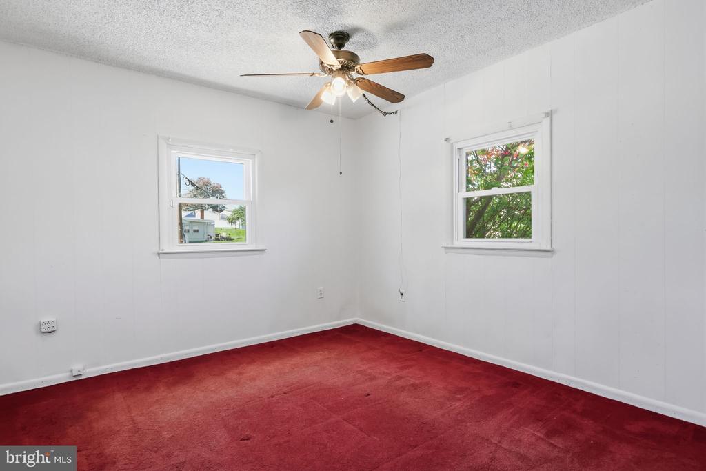 Empty room with red carpet, two windows, and a ceiling fan with light.
