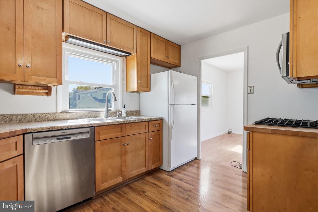 Kitchen with honey-colored wood cabinets, stainless steel dishwasher, white refrigerator, and gas cooktop.