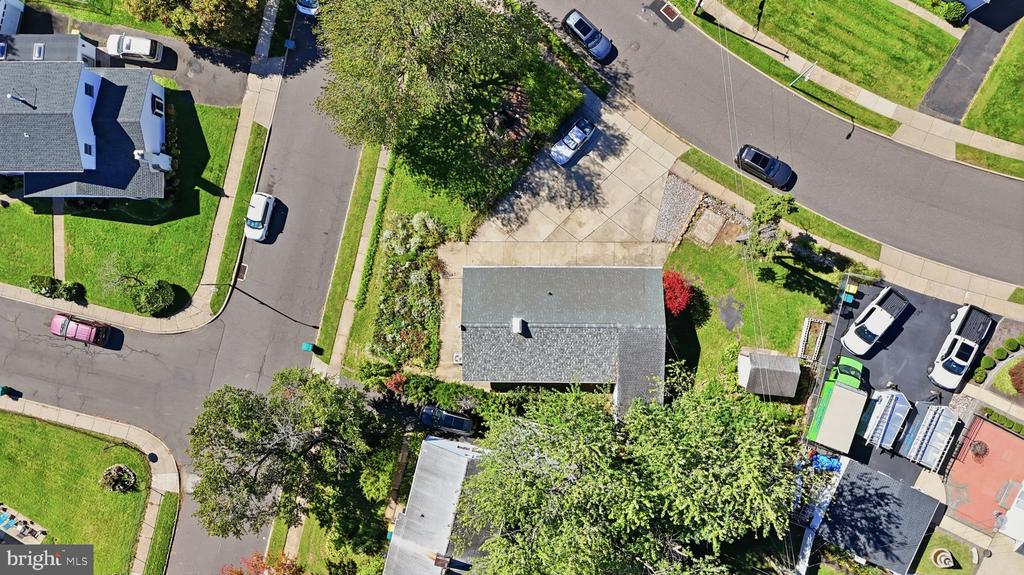 Aerial view of a home on a leafy street, with neighboring yards and parked cars.