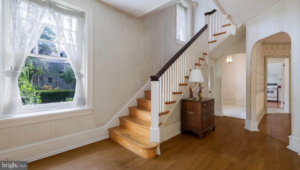 Entry foyer with hardwood floors, a wooden staircase, a curtained window, and an arched doorway.