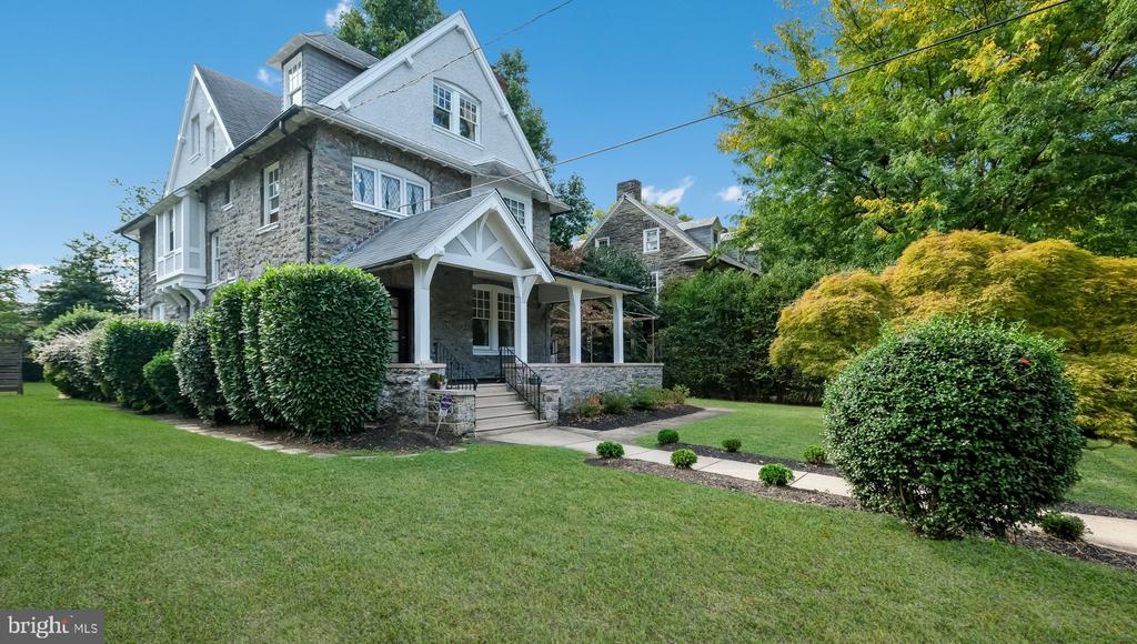 Stone house with white gables, a covered porch, and landscaped front lawn.