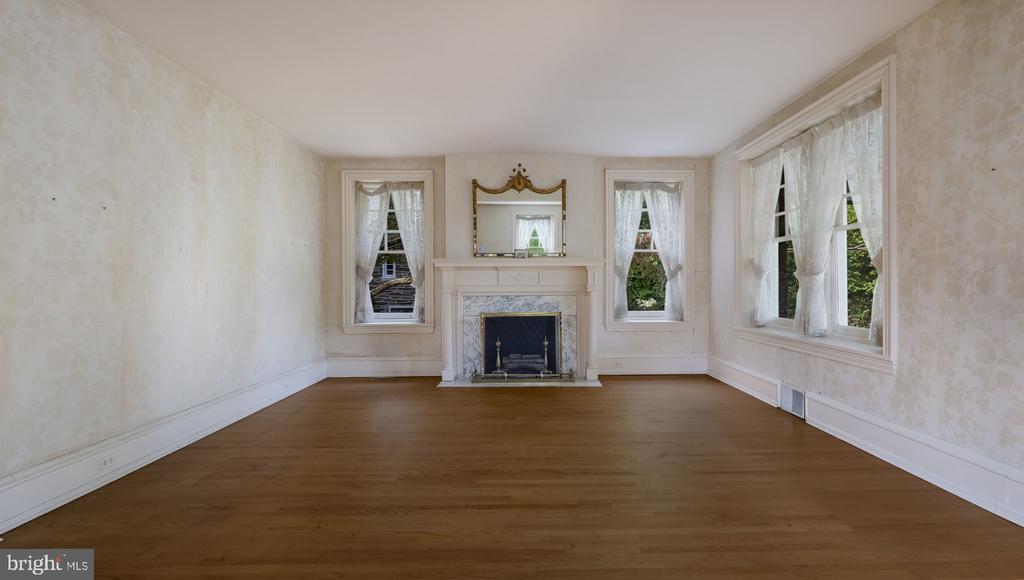 Vacant living room with hardwood floors, tall curtained windows, and a marble fireplace.