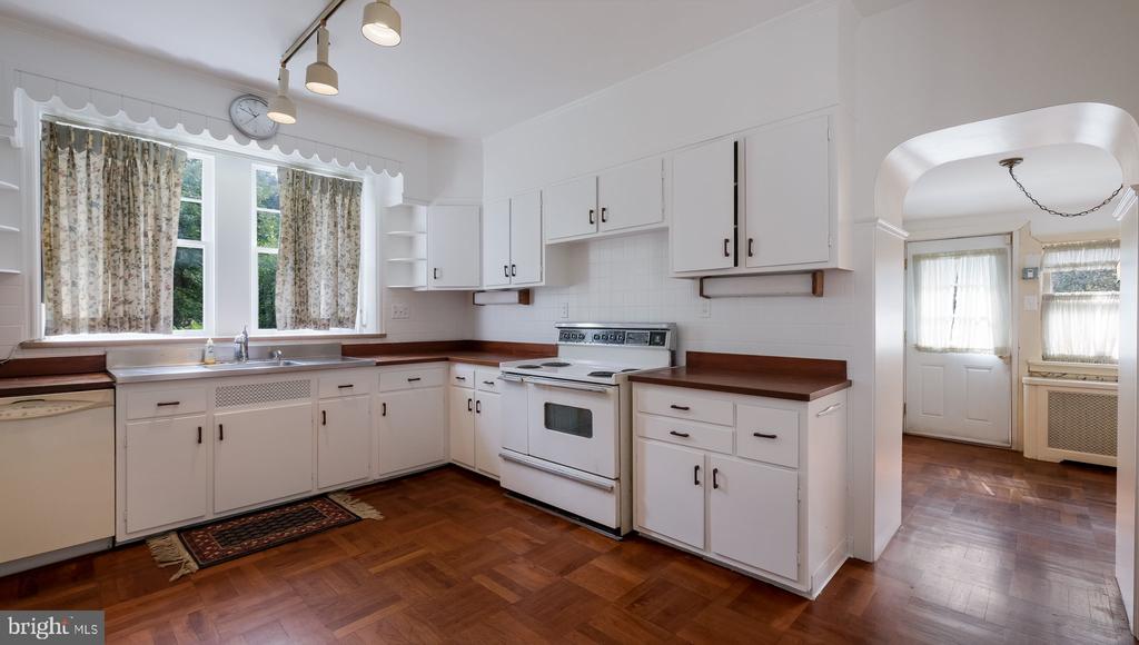 Kitchen with white cabinets, dark countertops, a window-side sink, and parquet flooring.