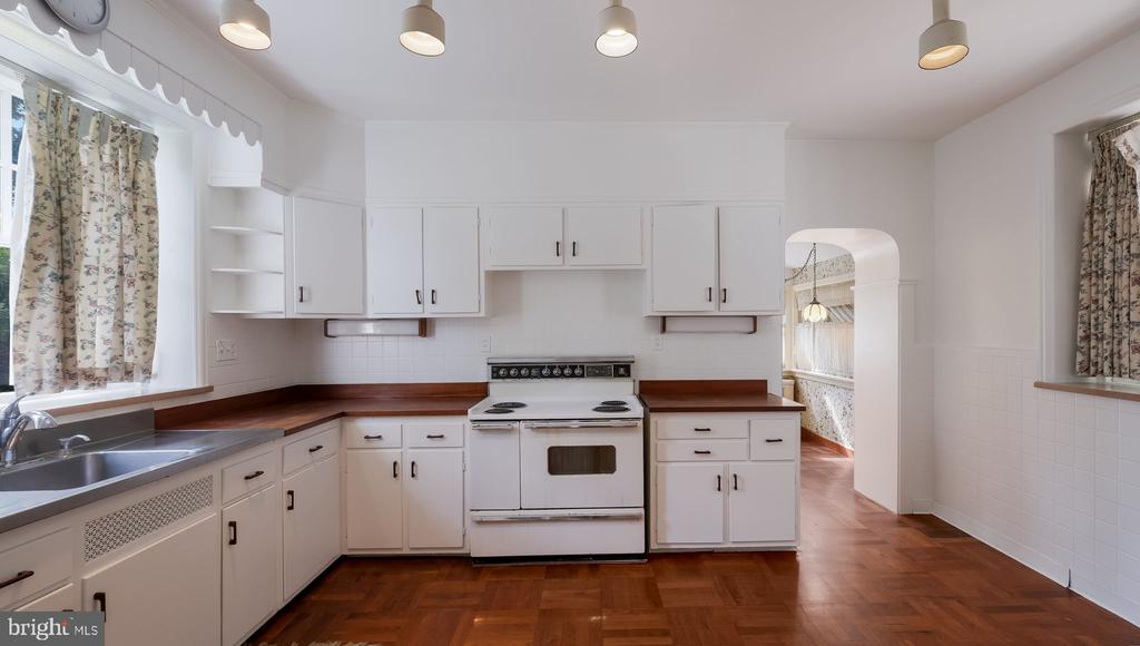 Kitchen with white cabinets, a freestanding range, floral curtains, and dark parquet flooring.