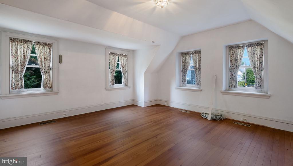 Vacant room with hardwood floors, a sloped ceiling, and four curtained windows.