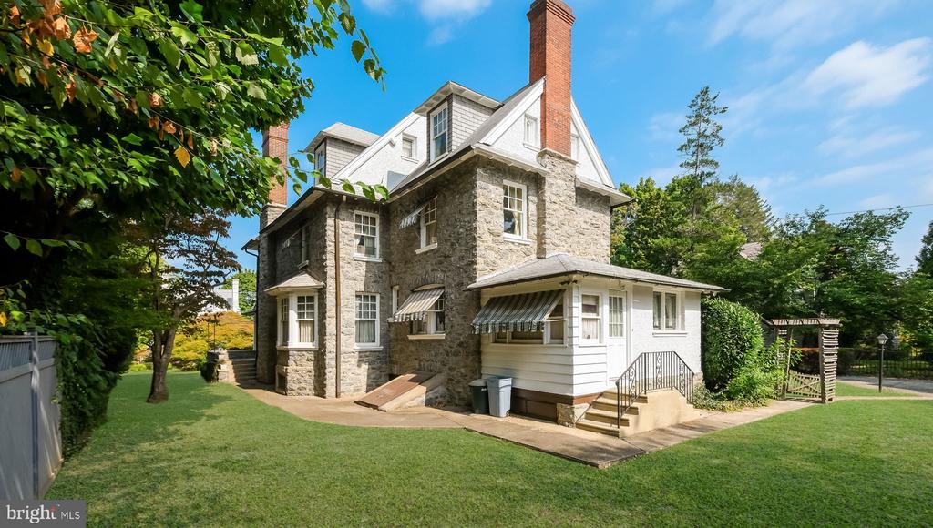 Stone house with white siding, striped awnings, and a broad lawn surrounded by mature trees.