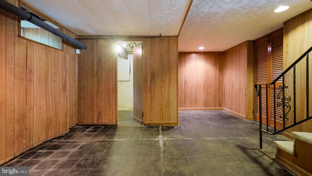 Empty wood-paneled basement with a dark concrete floor and decorative metal stair railing.