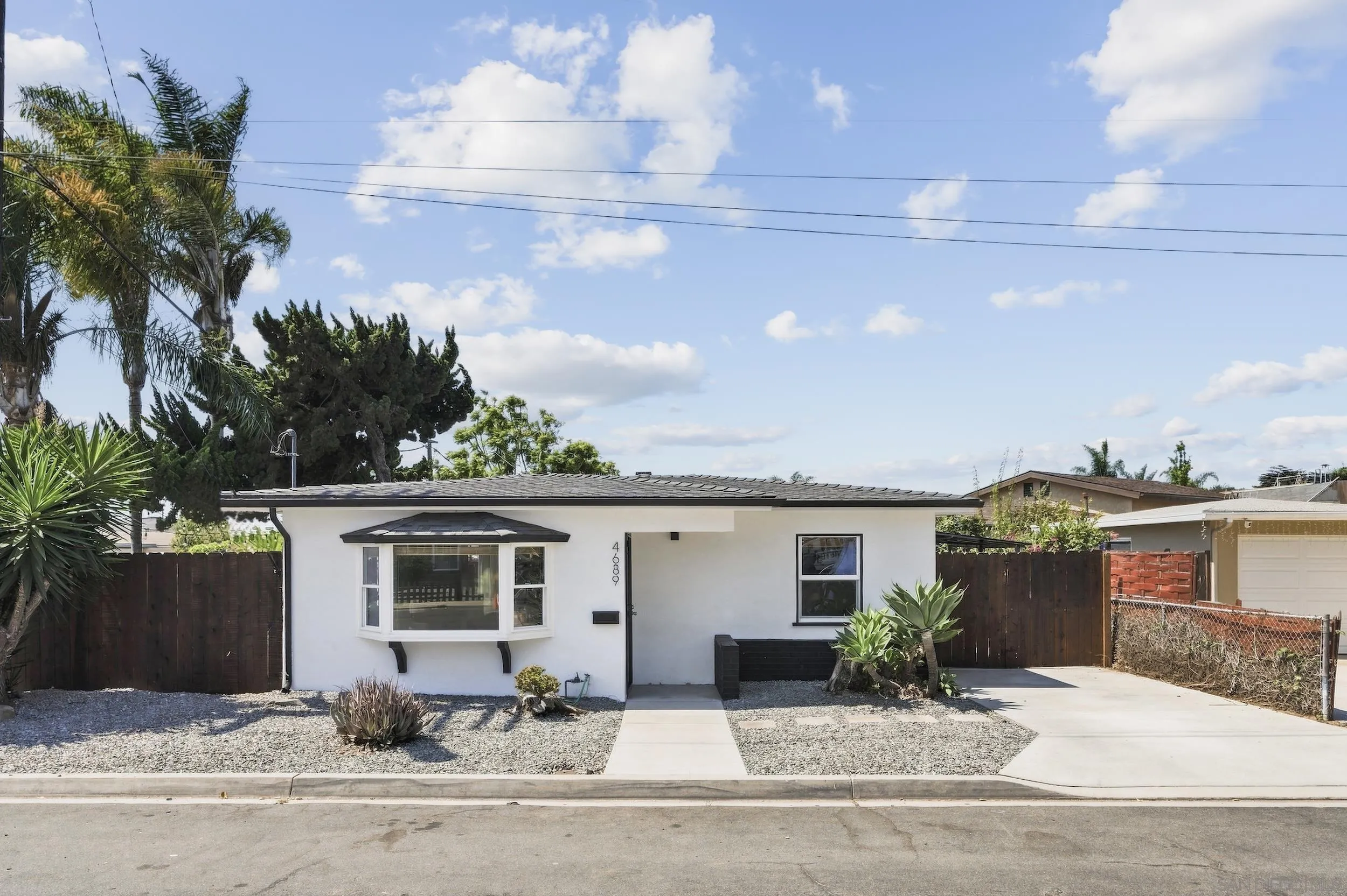 Single-story white house with a bay window, gravel landscaping, and a concrete driveway.