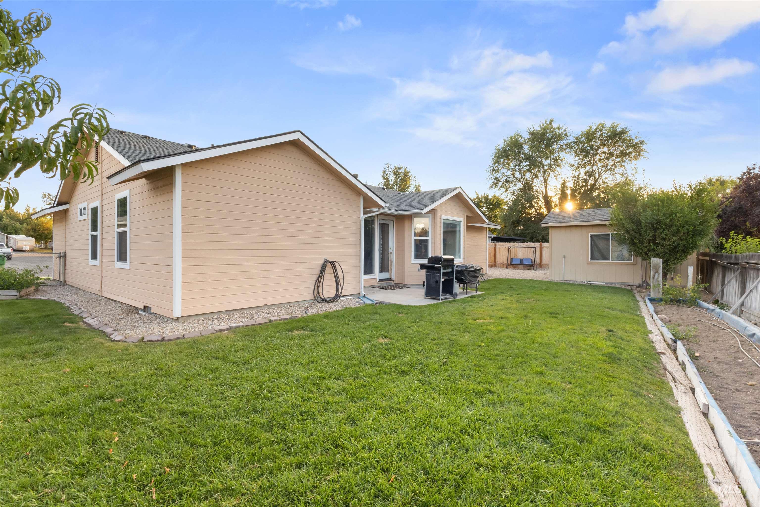 Tan-sided home and patio grill beyond a broad lawn, with a detached outbuilding in the fenced backyard.