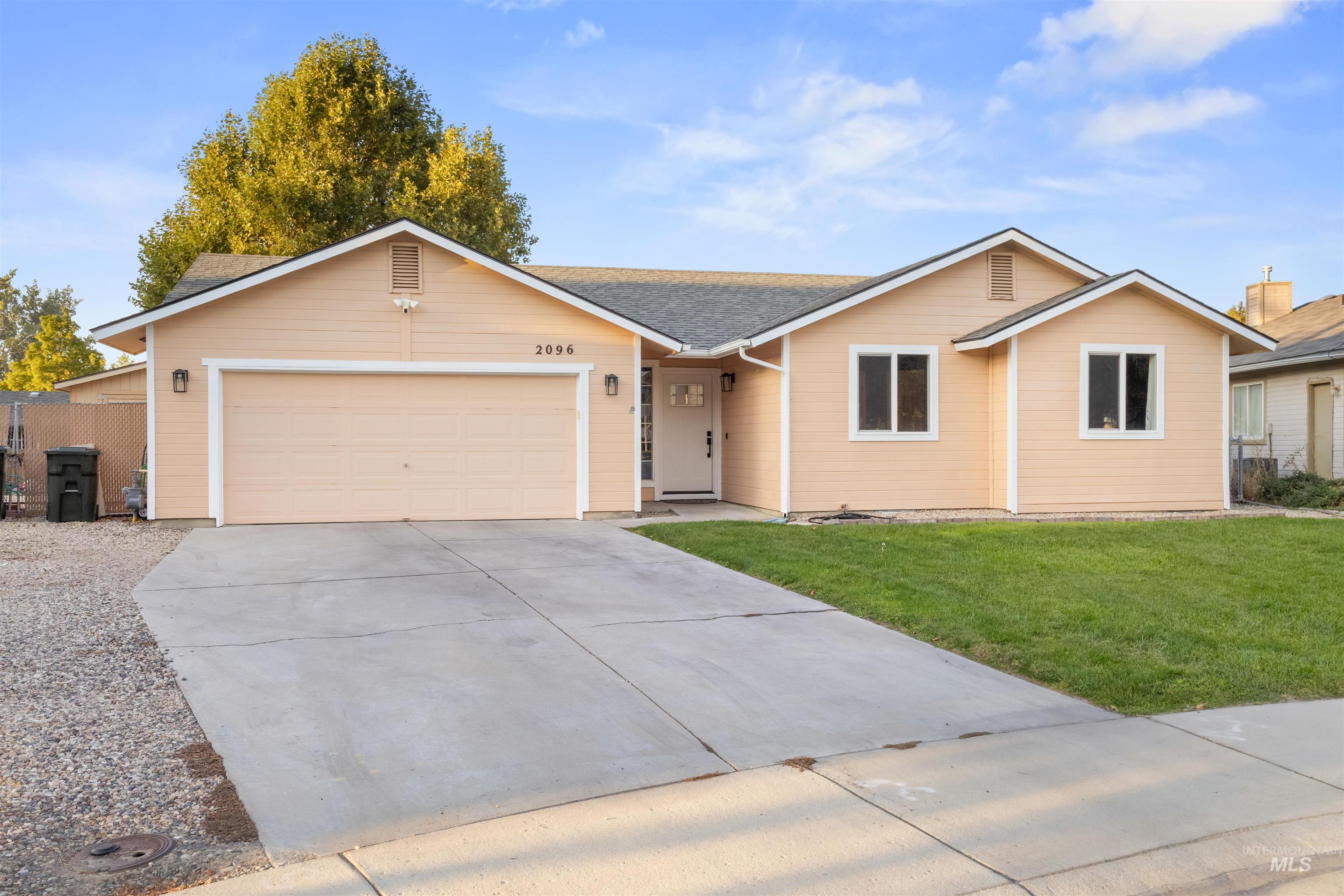 Peach single-story house with white trim, a two-car garage, and a wide concrete driveway.