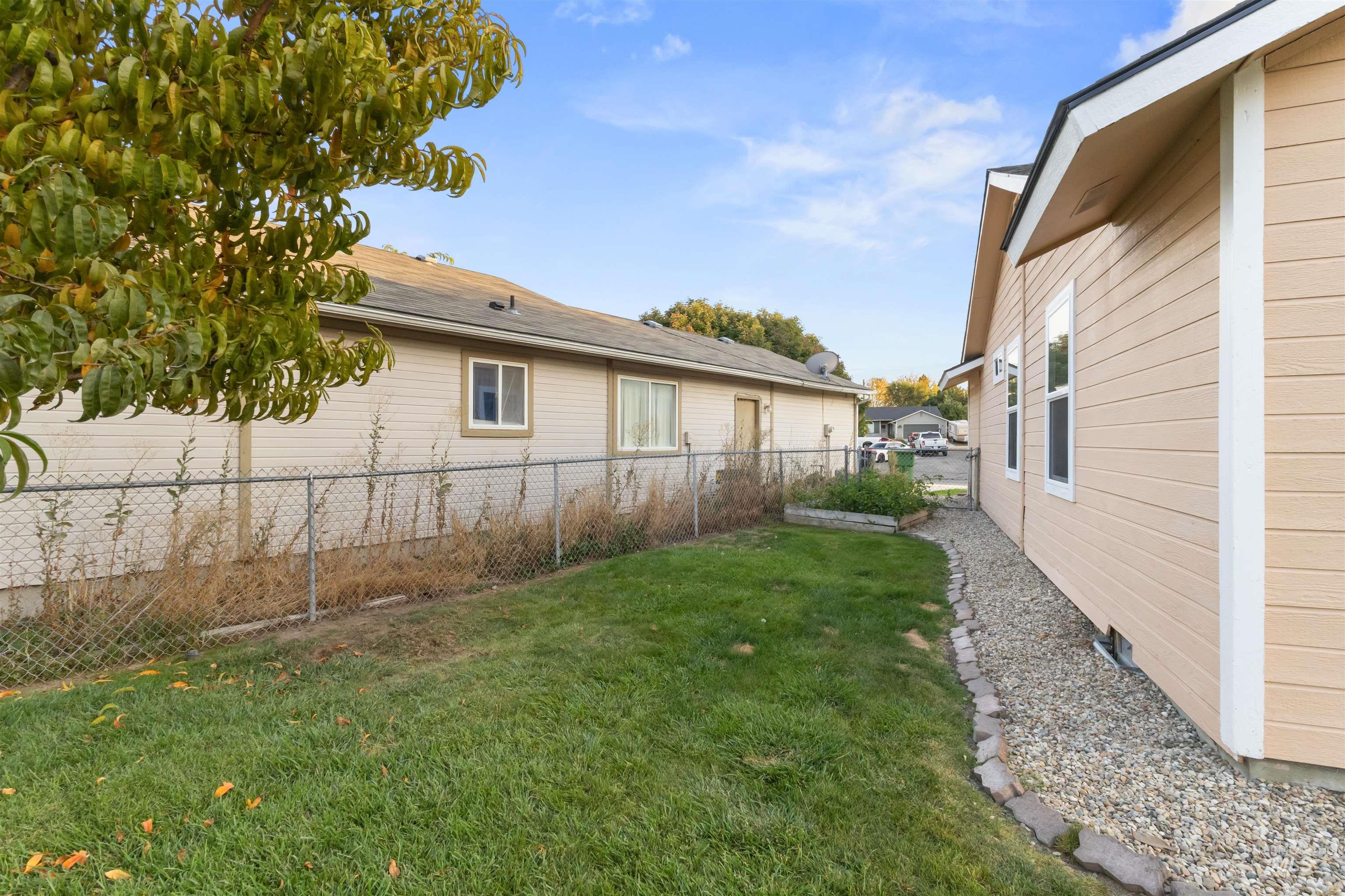 Grassy backyard between beige homes, with a chain-link fence and gravel border.