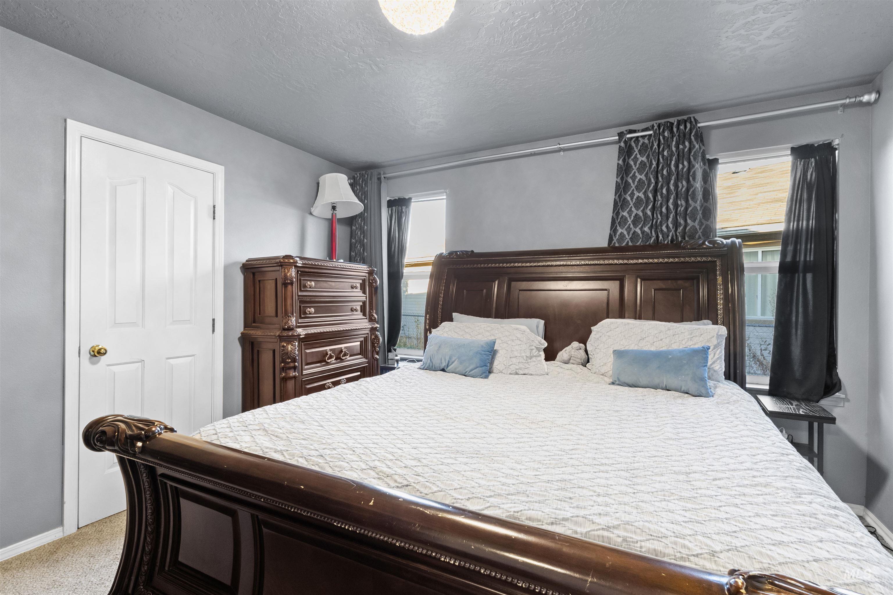 Bedroom with an ornate dark wood bed, white bedding, blue pillows, and matching dresser.