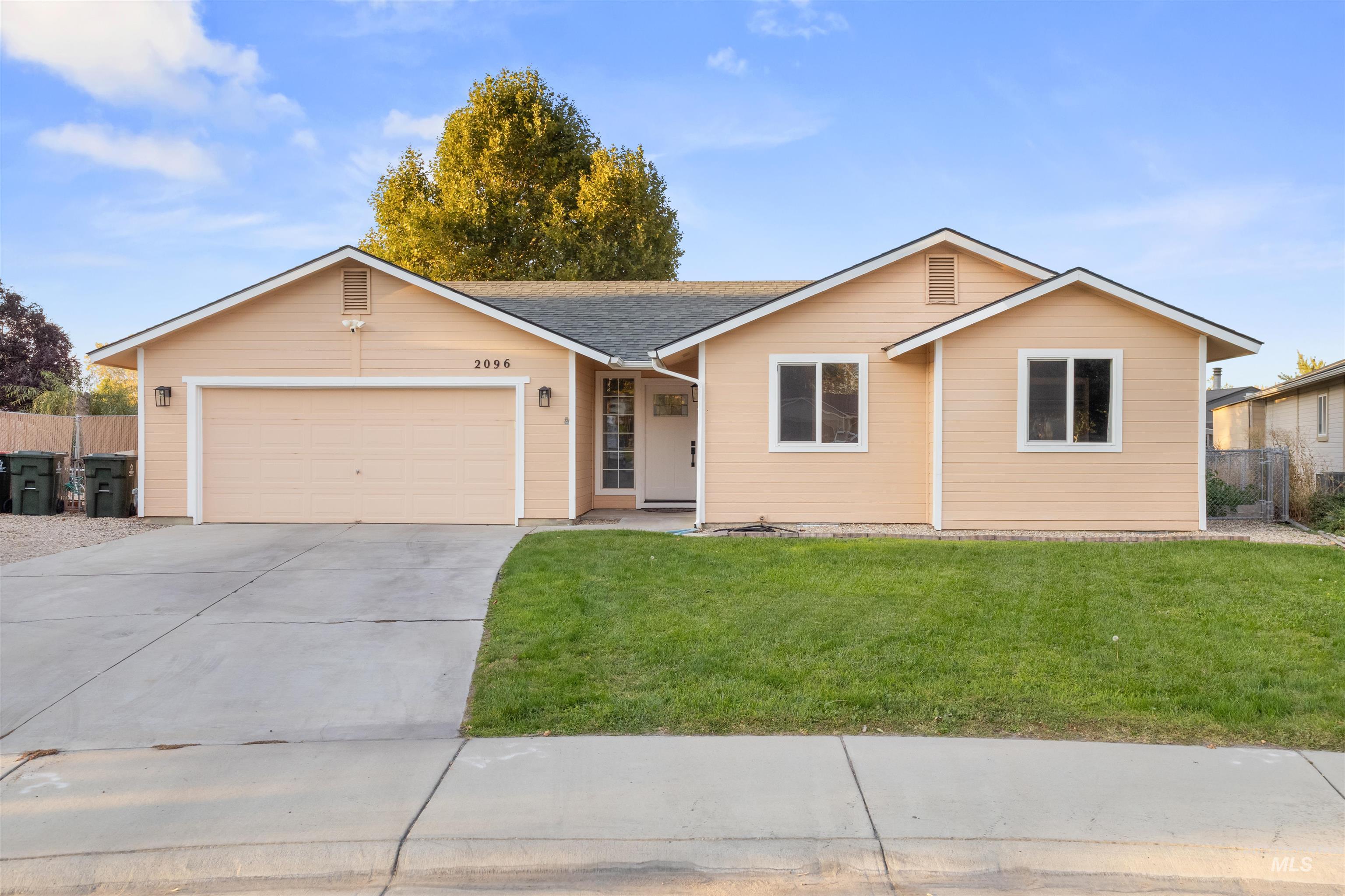 Peach single-story house with a two-car garage, wide driveway, and autumn tree behind it.