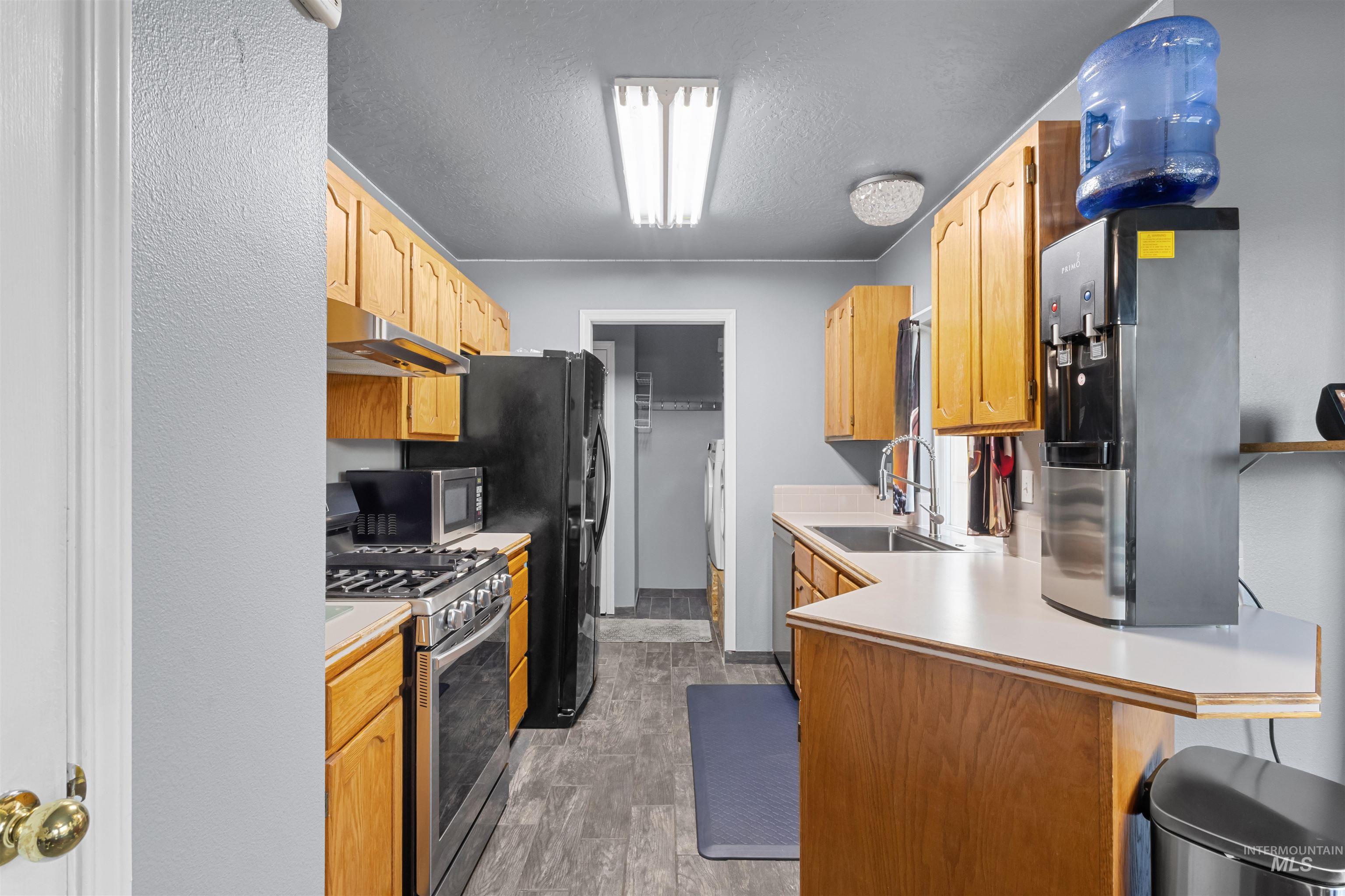 Kitchen with honey-colored cabinets, dark appliances, and a long counter with a double sink.