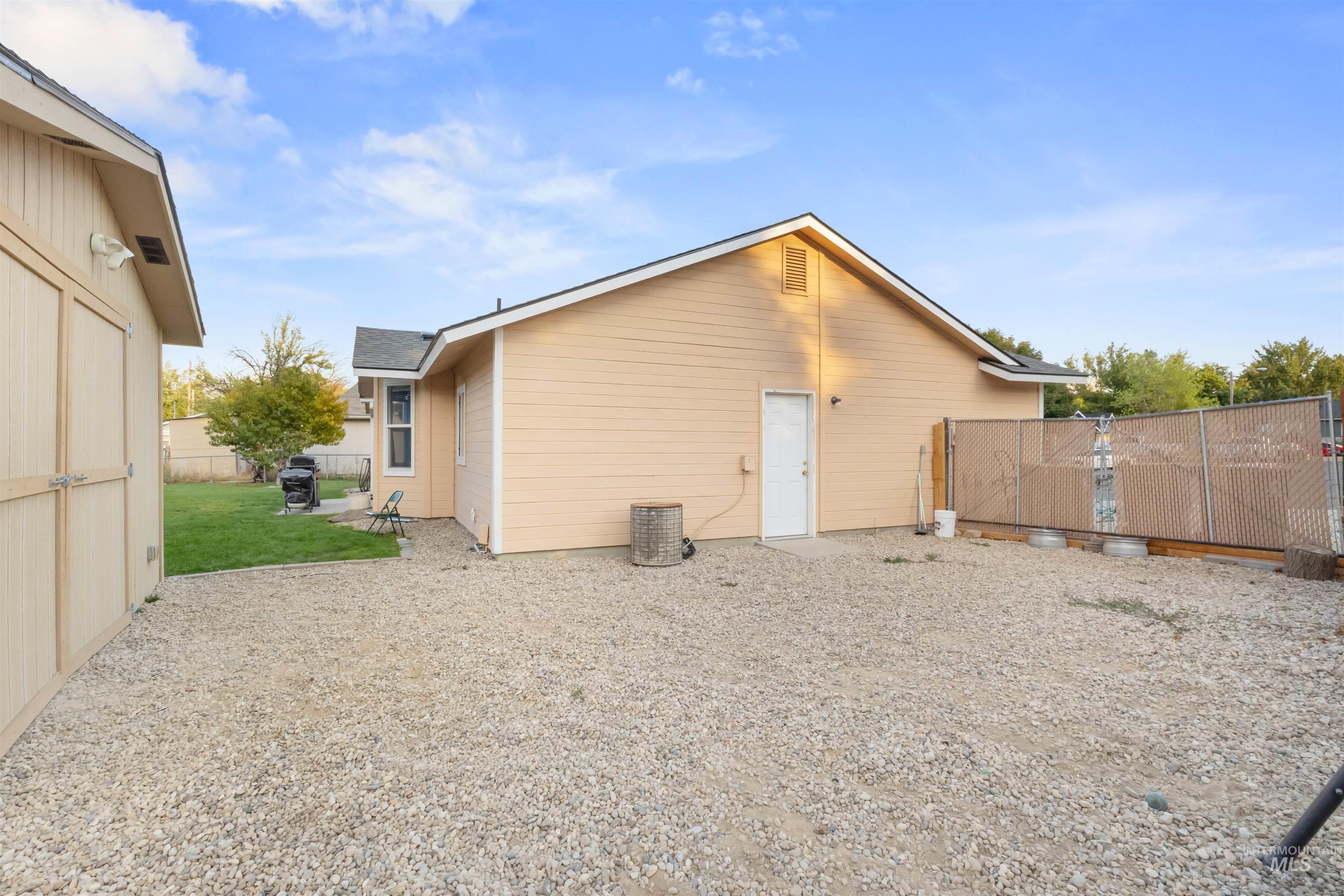 Tan outbuilding with a white door, gravel yard, and chain-link fence.