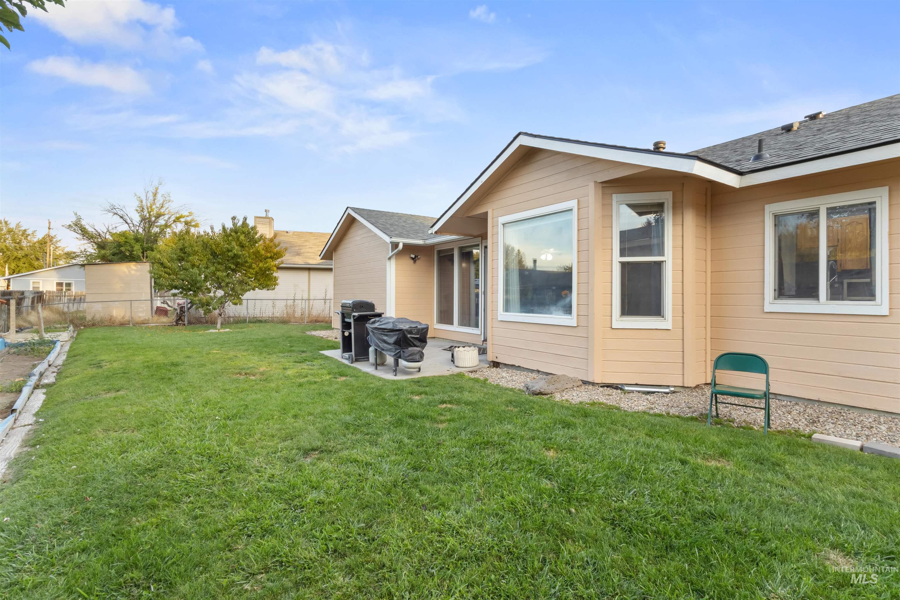 Tan-sided house behind a broad green lawn, with grills on the patio and a fenced backyard.
