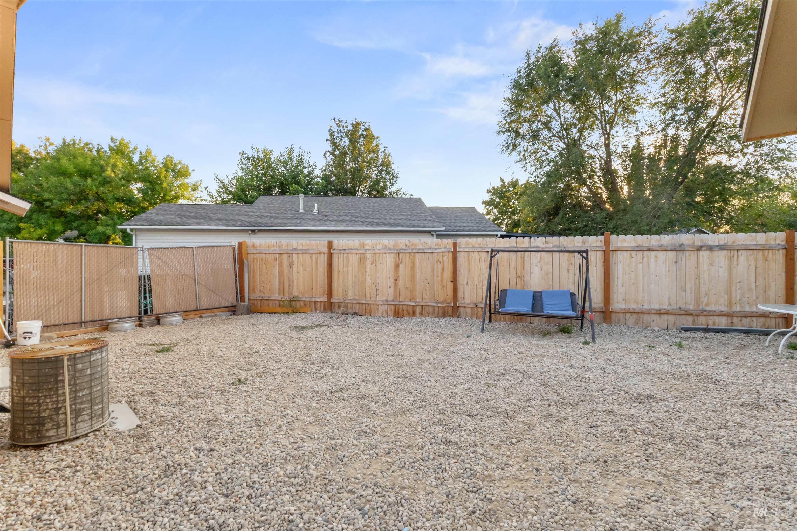 Gravel-covered fenced backyard with a wooden swing and mature trees.