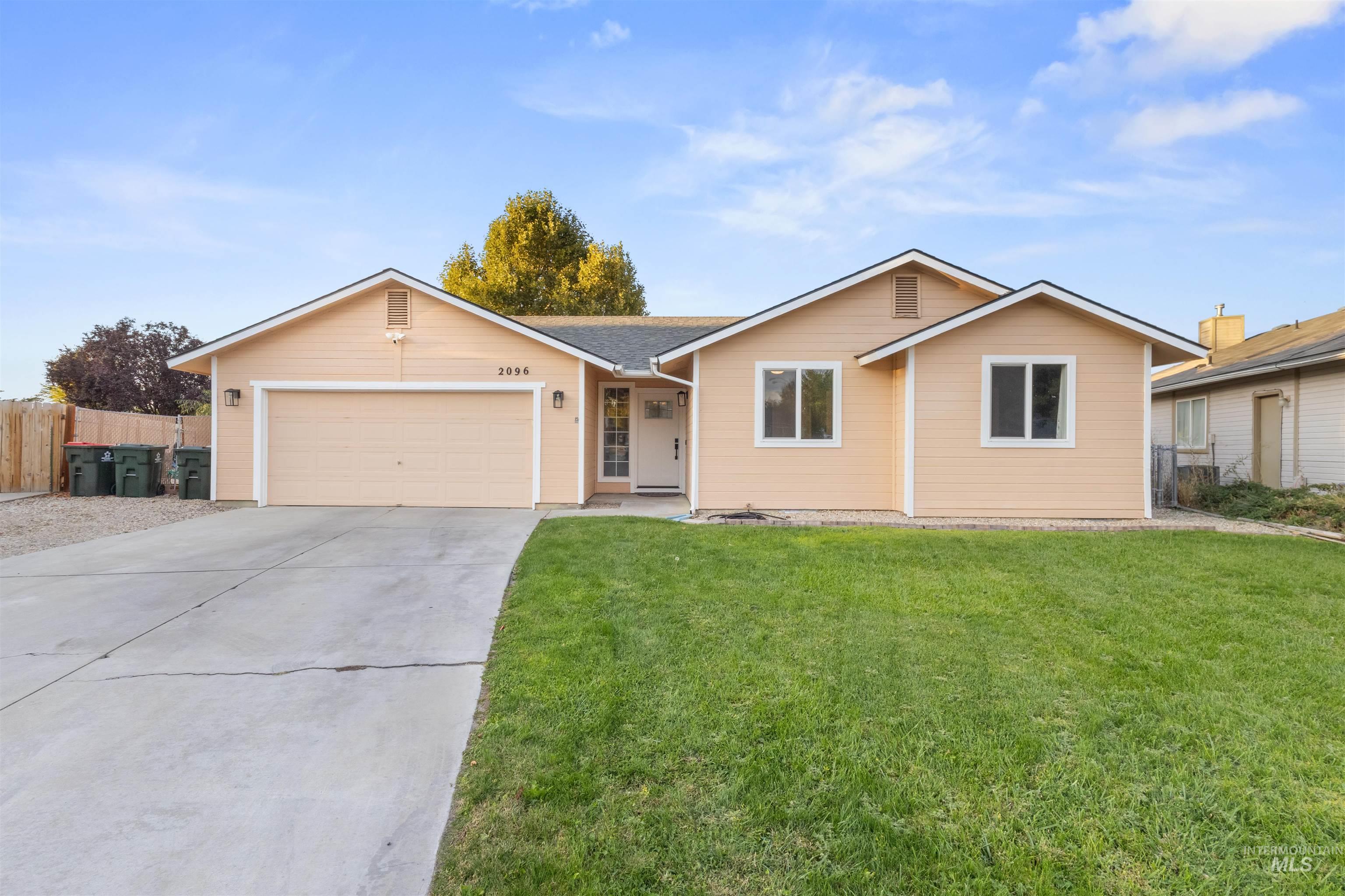 Peach single-story house with a two-car garage, broad driveway, and green front lawn.