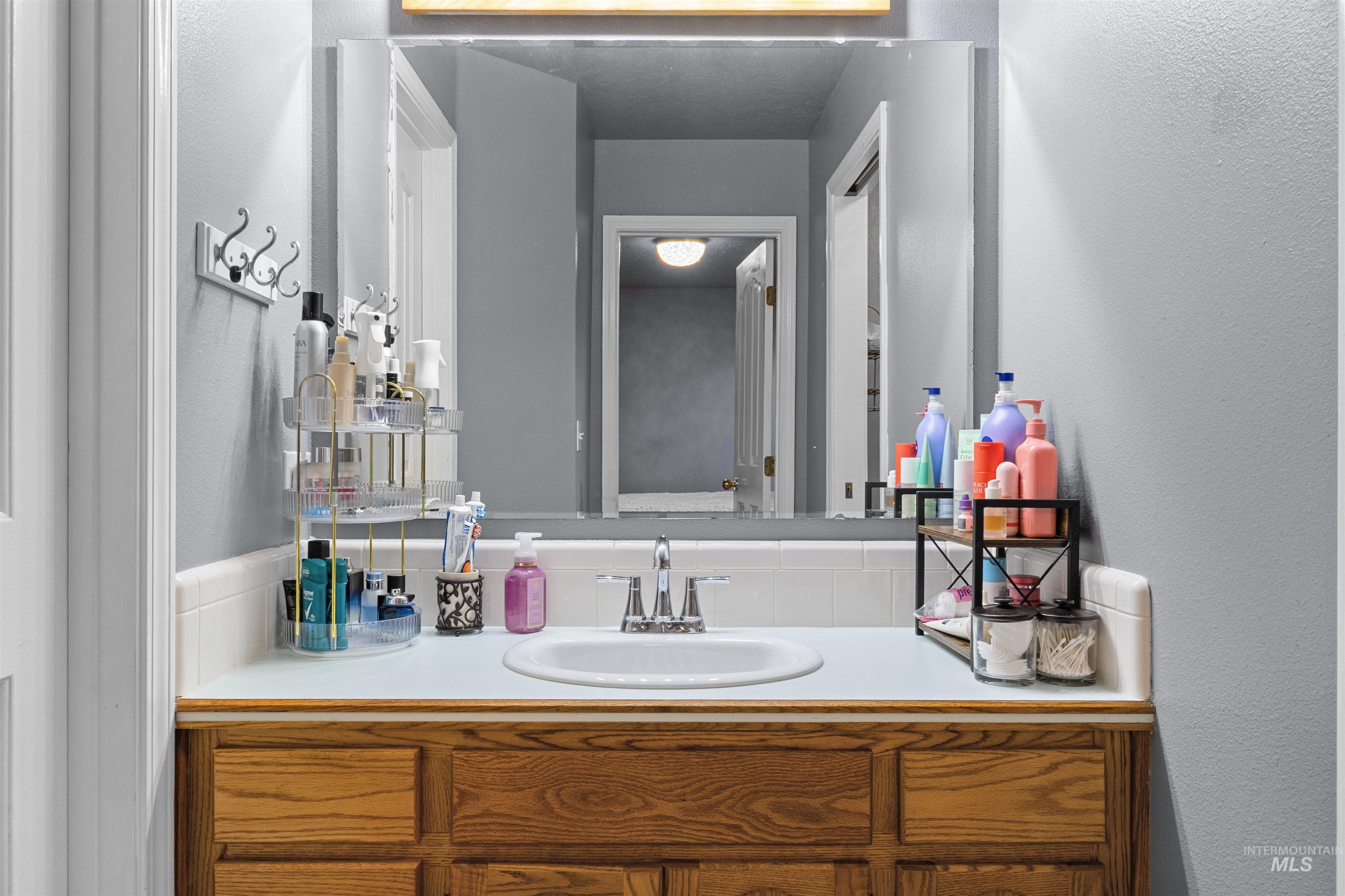 Bathroom vanity with a large mirror, oval sink, wood cabinetry, and toiletries on the counter.