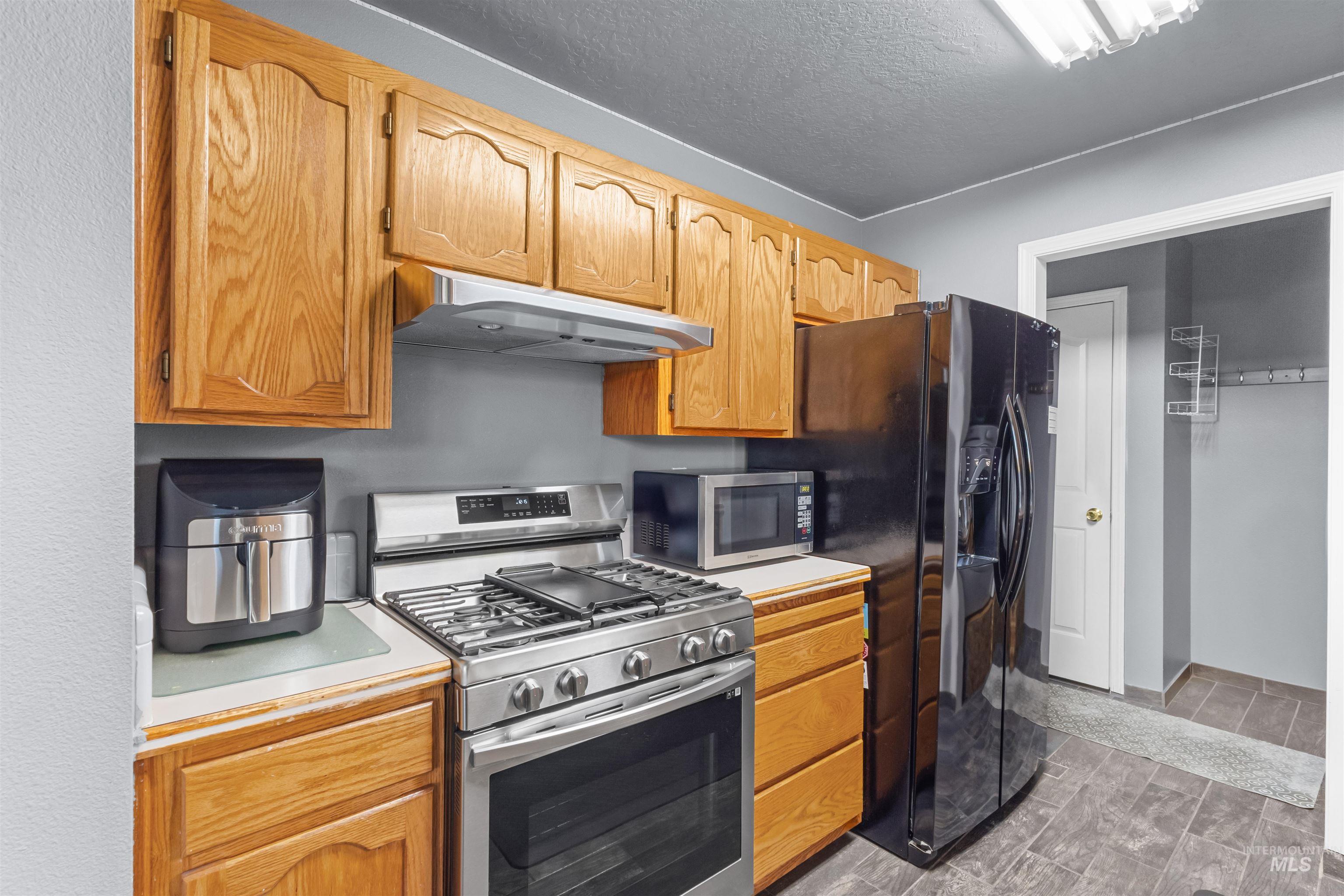 Kitchen with oak cabinets, stainless-steel gas range and microwave, and a black refrigerator.