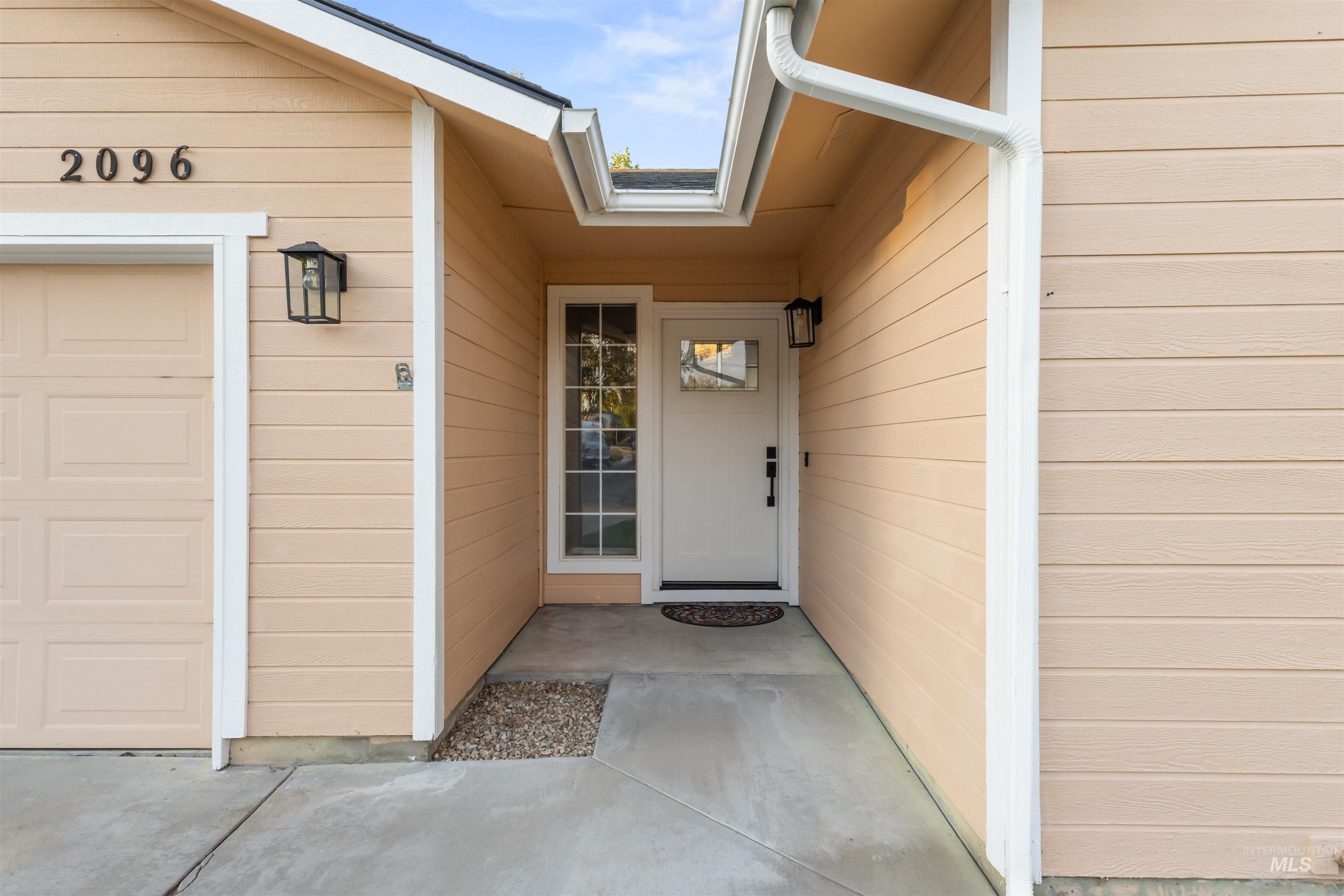 Covered front entry with a white door and sidelight beside a garage.