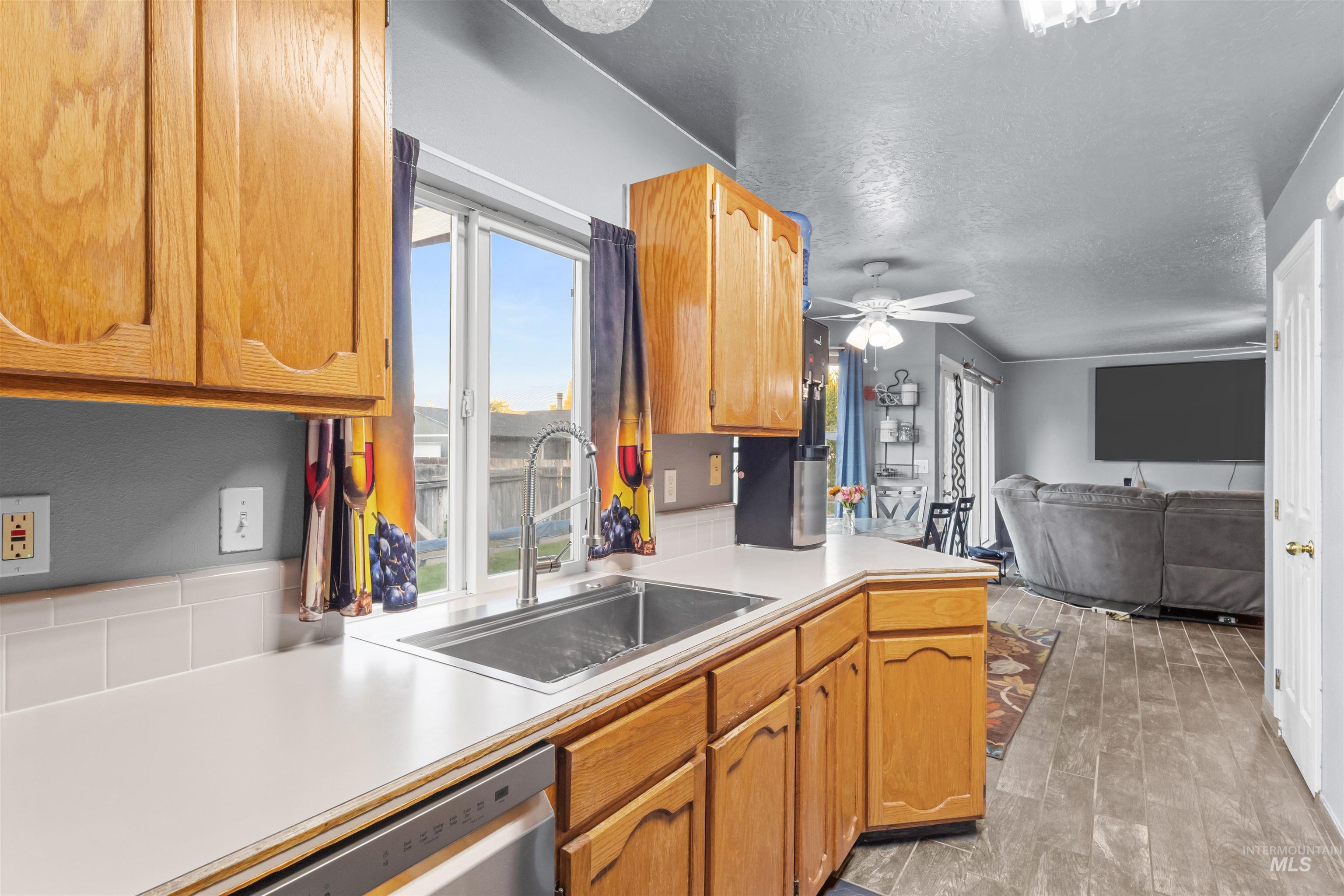 Kitchen with honey-colored cabinets and a window sink, opening onto a living room with a gray sectional.