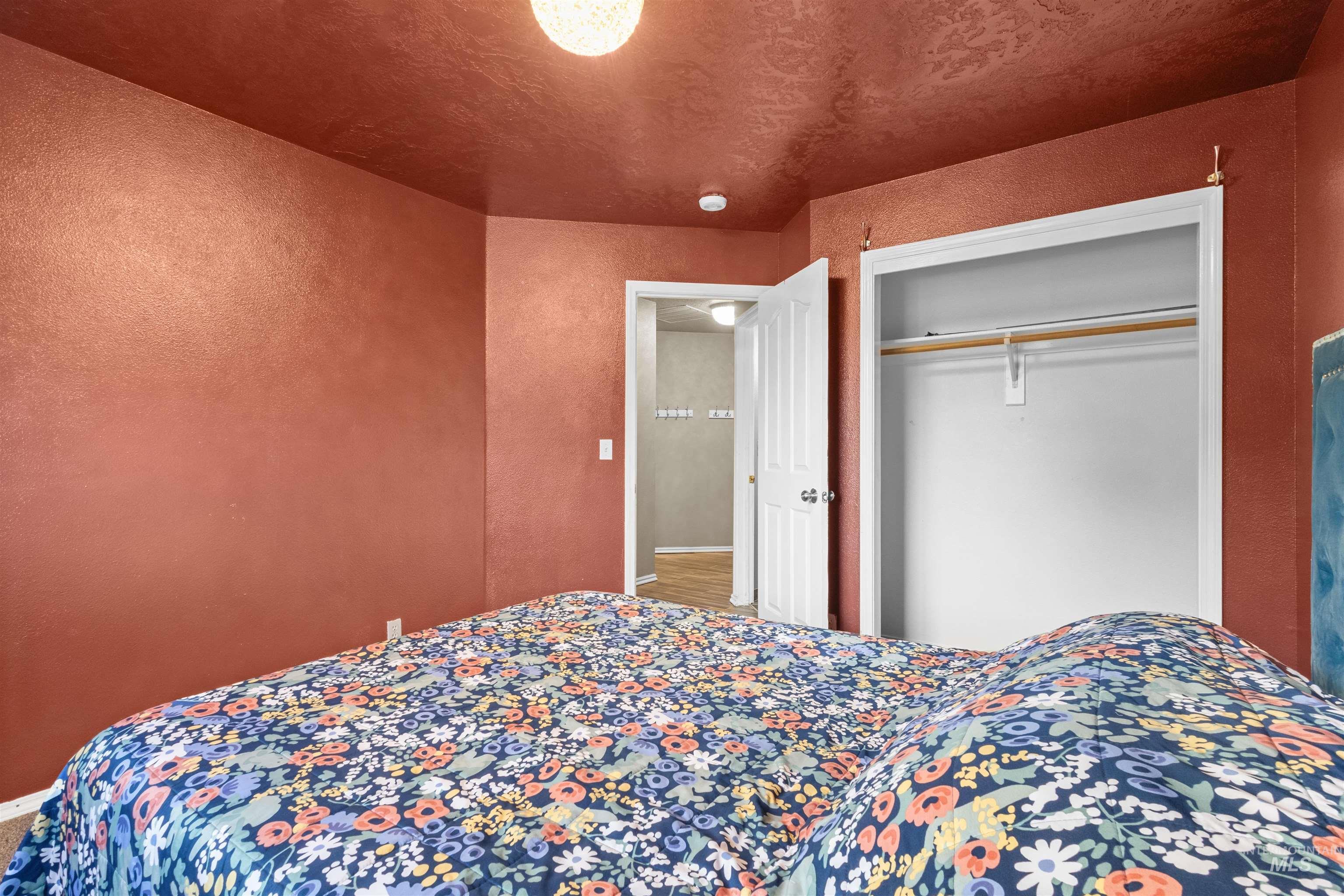 Bedroom with rust-red walls, a blue floral bedspread, and an open closet.